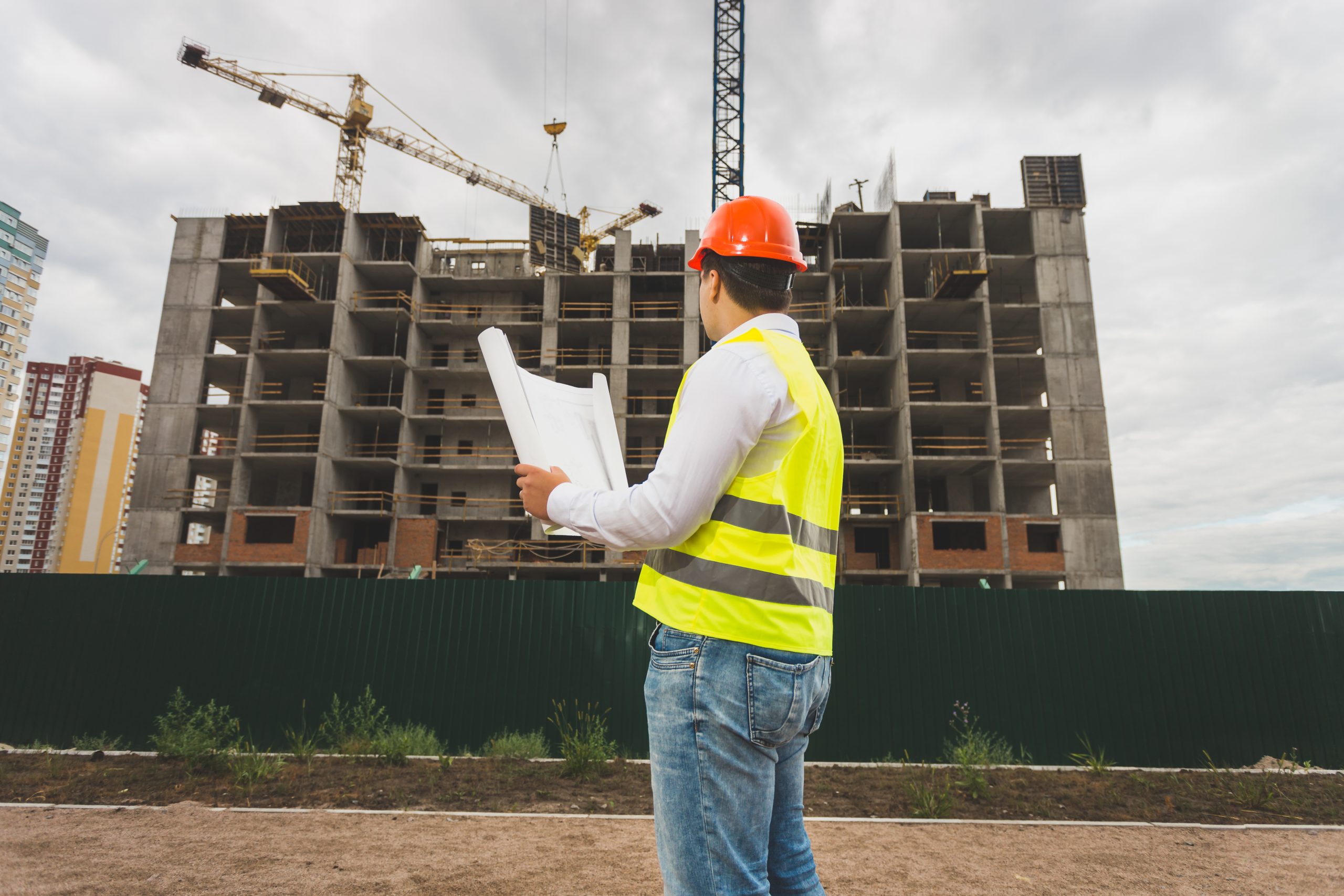 Toned image of engineer in hardhat and vest inspecting building site