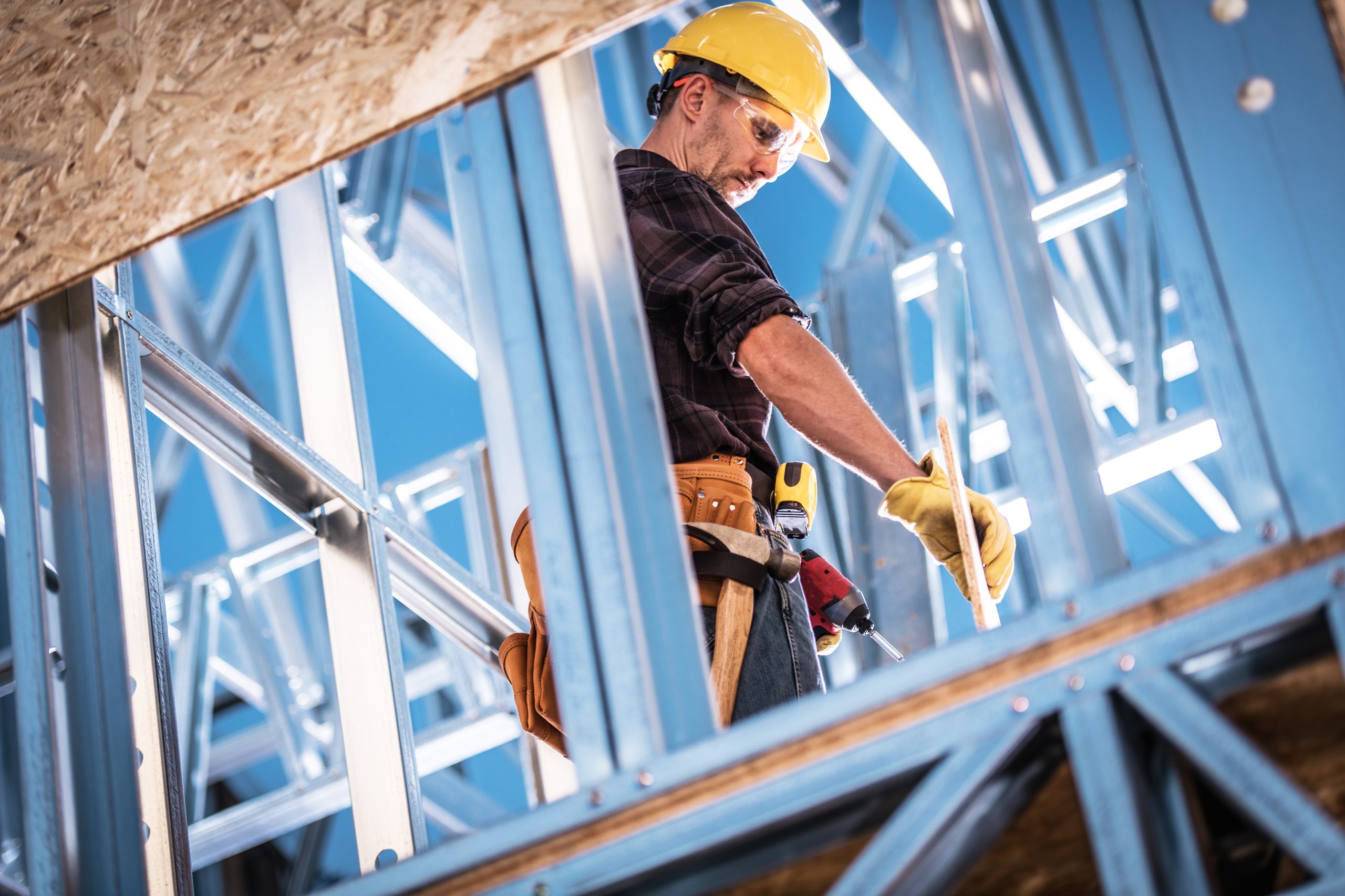 Caucasian Worker and the Construction Site. Skeleton Steel Frame of the Building. Hard hat Zone.